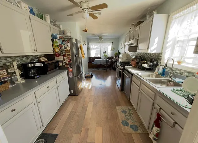 a kitchen with a sink dishwasher stove and white cabinets with wooden floor