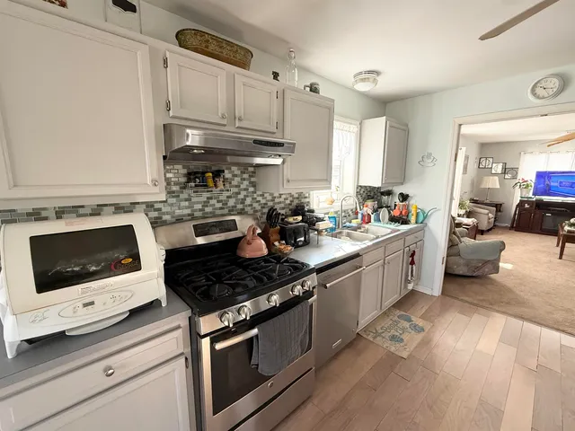 a kitchen with stainless steel appliances a stove a sink cabinets and a view of living room