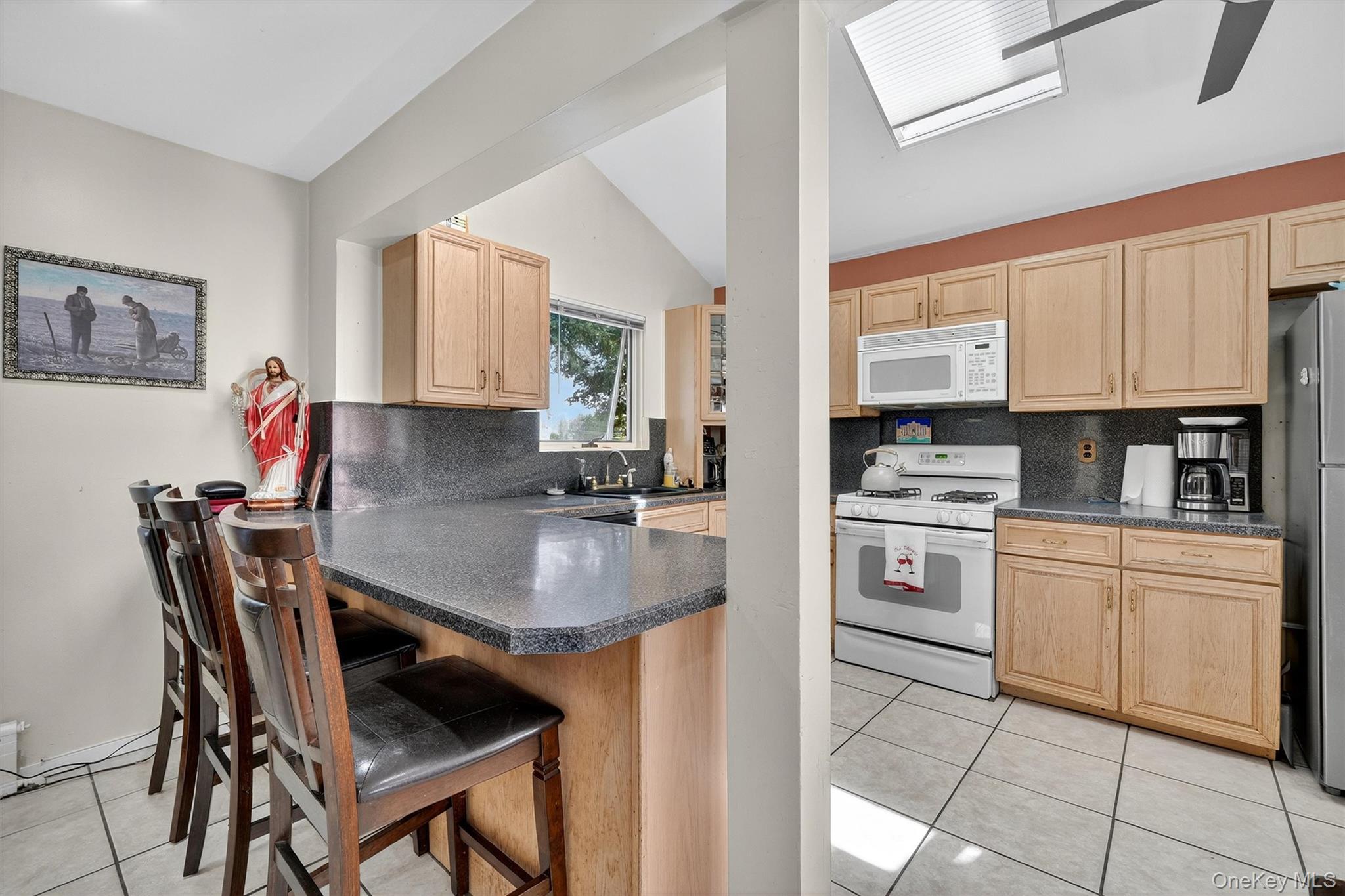 3384 Country Club Road Bronx, NY 10465 - Photo 12 of 48 Kitchen with light brown cabinets, light tile patterned flooring, white appliances, decorative backsplash, and lofted ceiling