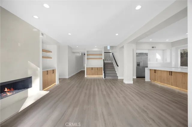 a view of an empty room with wooden floor and a kitchen