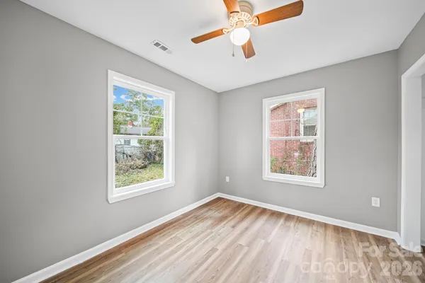 an empty room with wooden floor chandelier fan and windows