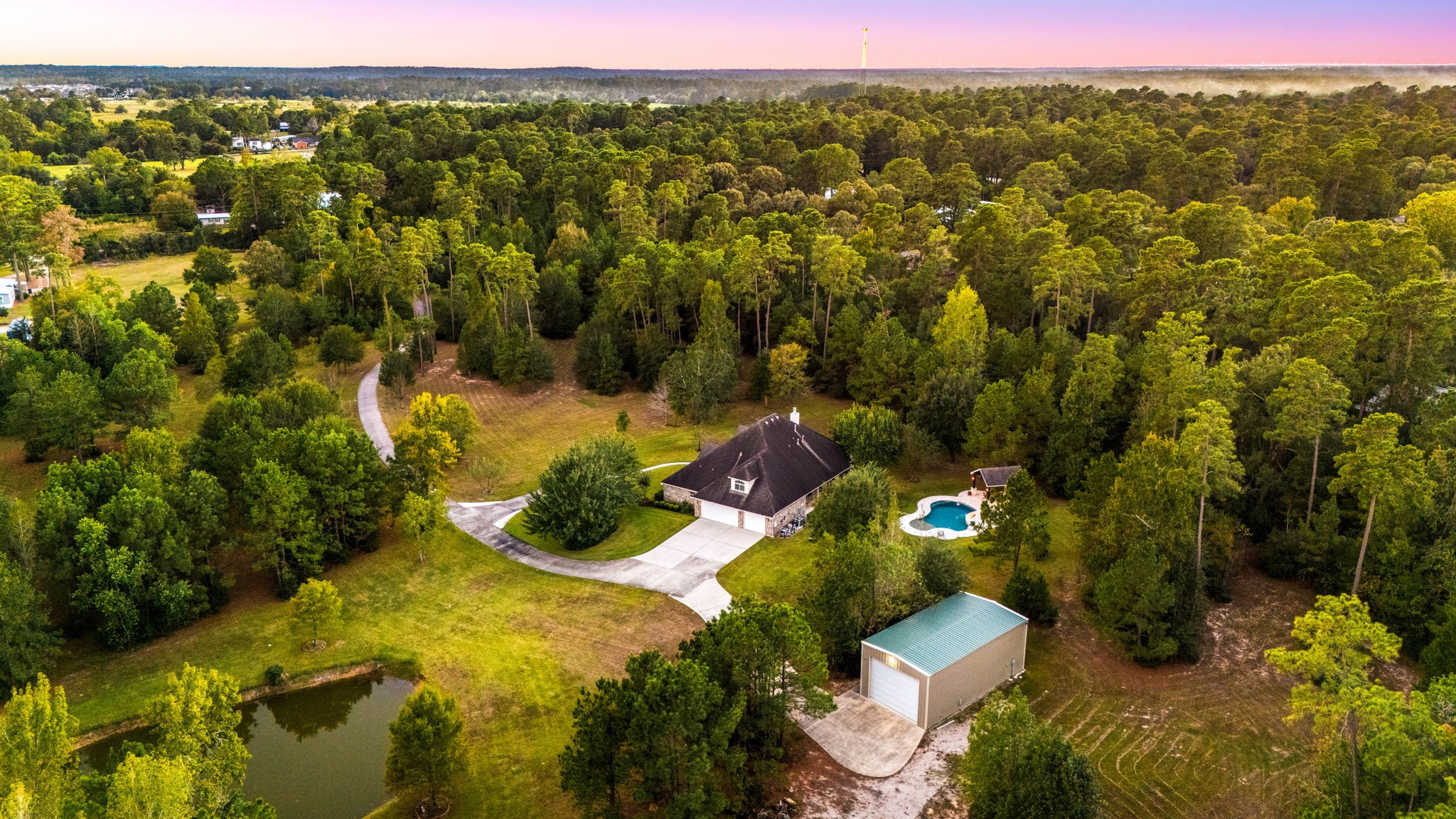 This stunning aerial view showcases the full beauty of the property, lush trees framing expansive green space, a sparkling pool, and a covered outdoor pavilion. The layout offers privacy, tranquility, and a true sense of country living, all within a beautifully maintained setting.