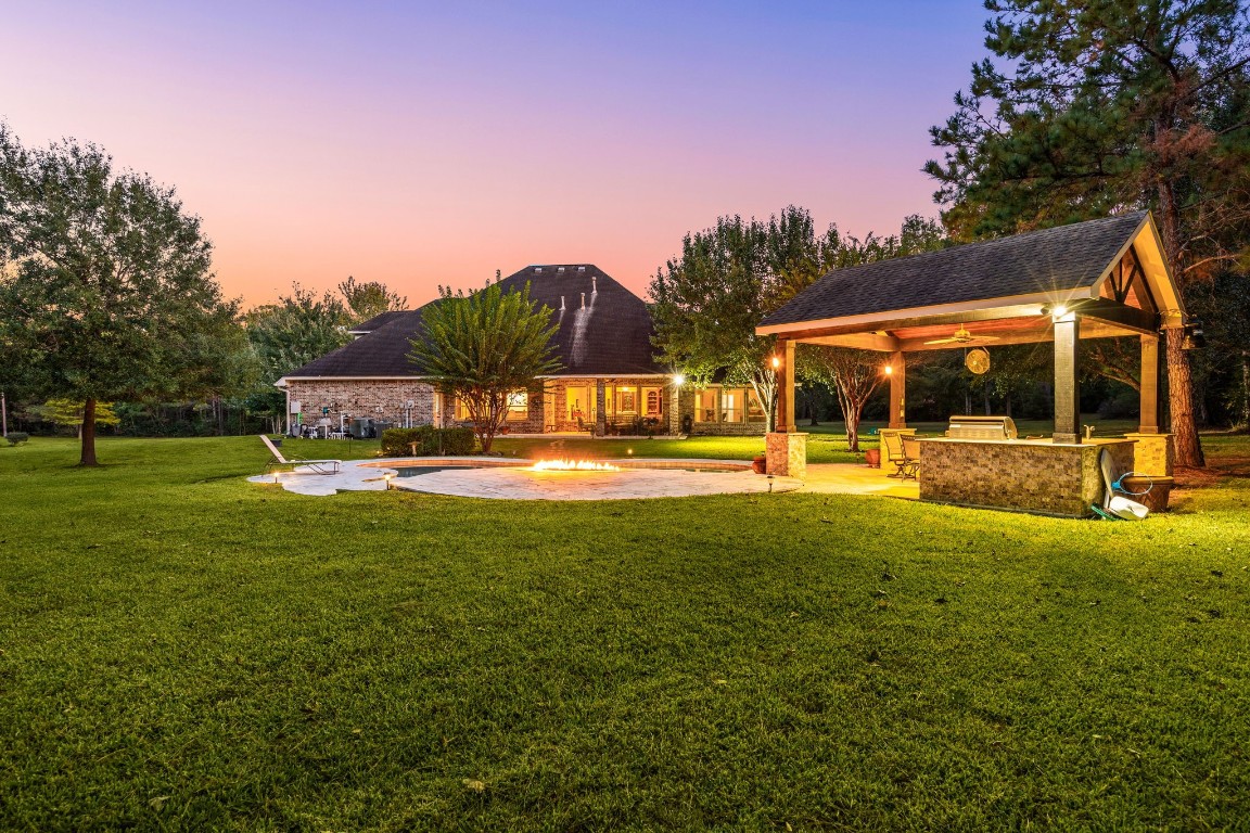 13506 Stagecoach Road Magnolia, TX 77355 - Photo 32 of 37 Step into a private outdoor escape where every detail invites relaxation and connection. A shimmering pool and glowing fire feature anchor the space, while the covered pavilion with a full outdoor kitchen makes entertaining effortless. Surrounded by mature trees and open lawn, this backyard offers an ideal balance of comfort and sophistication.