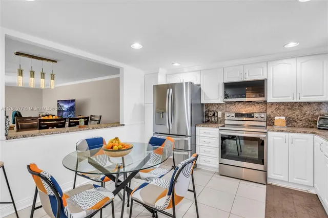 a kitchen with stainless steel appliances a stove a sink dishwasher a refrigerator with a dining table and chairs