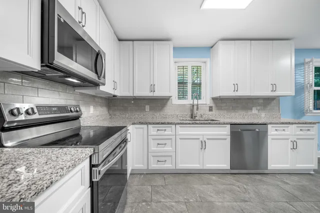 a kitchen with granite countertop white cabinets stainless steel appliances a sink and a window