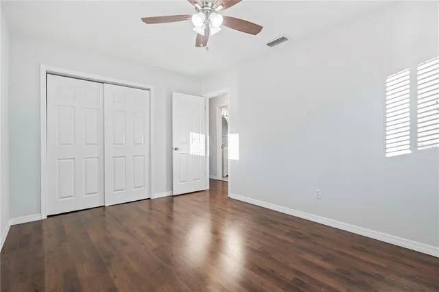 an empty room with wooden floor chandelier fan and windows