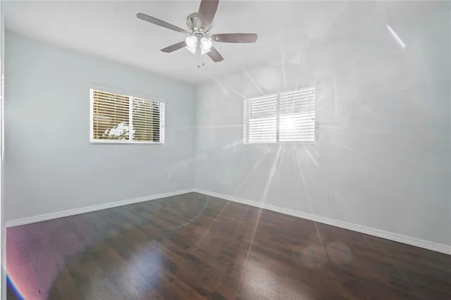 an empty room with wooden floor ceiling fan and windows
