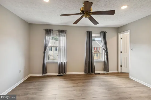 an empty room with wooden floor fan and windows