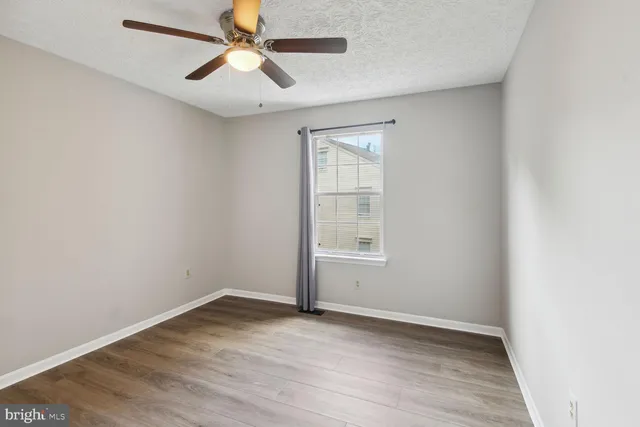 an empty room with wooden floor ceiling fan and windows