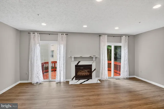 a view of an empty room with wooden floor fireplace and a window