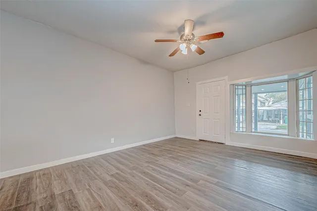 a view of an empty room with chandelier fan and wooden floor