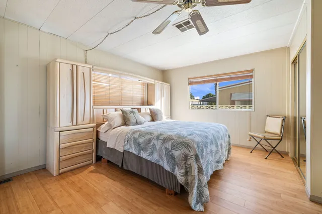 a bedroom with a bed a chair and potted plant on the dresser