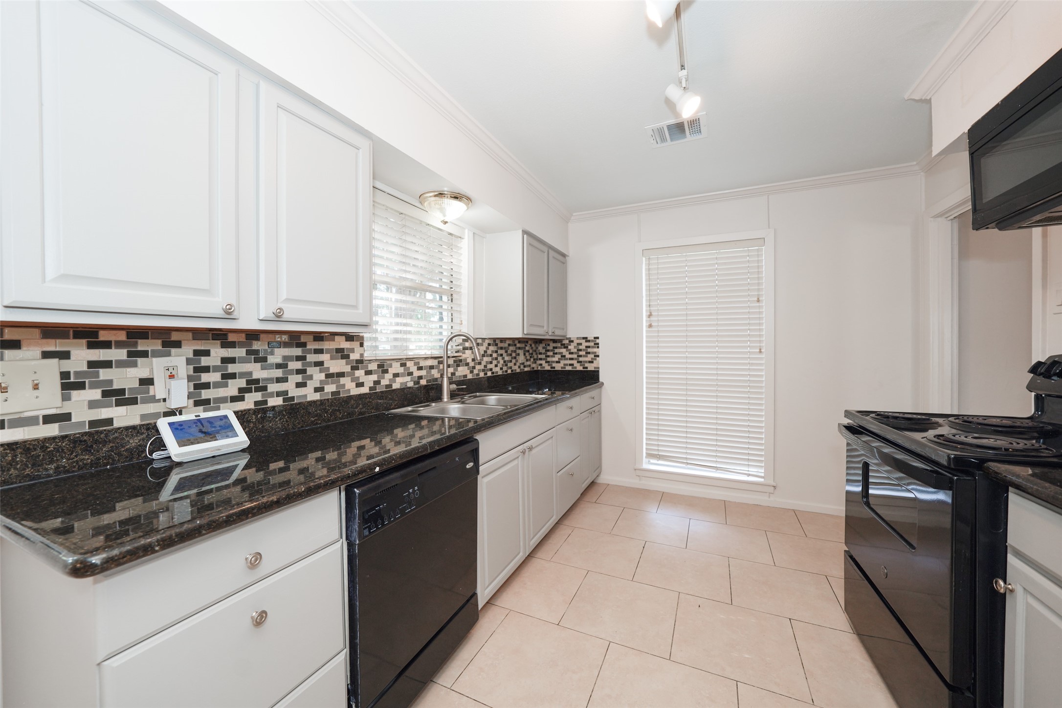 9519 Val Verde Street Houston, TX 77063 - Photo 11 of 27 This kitchen features sleek black appliances, white cabinetry, and a modern tile backsplash. It has granite countertops and large windows providing plenty of natural light.