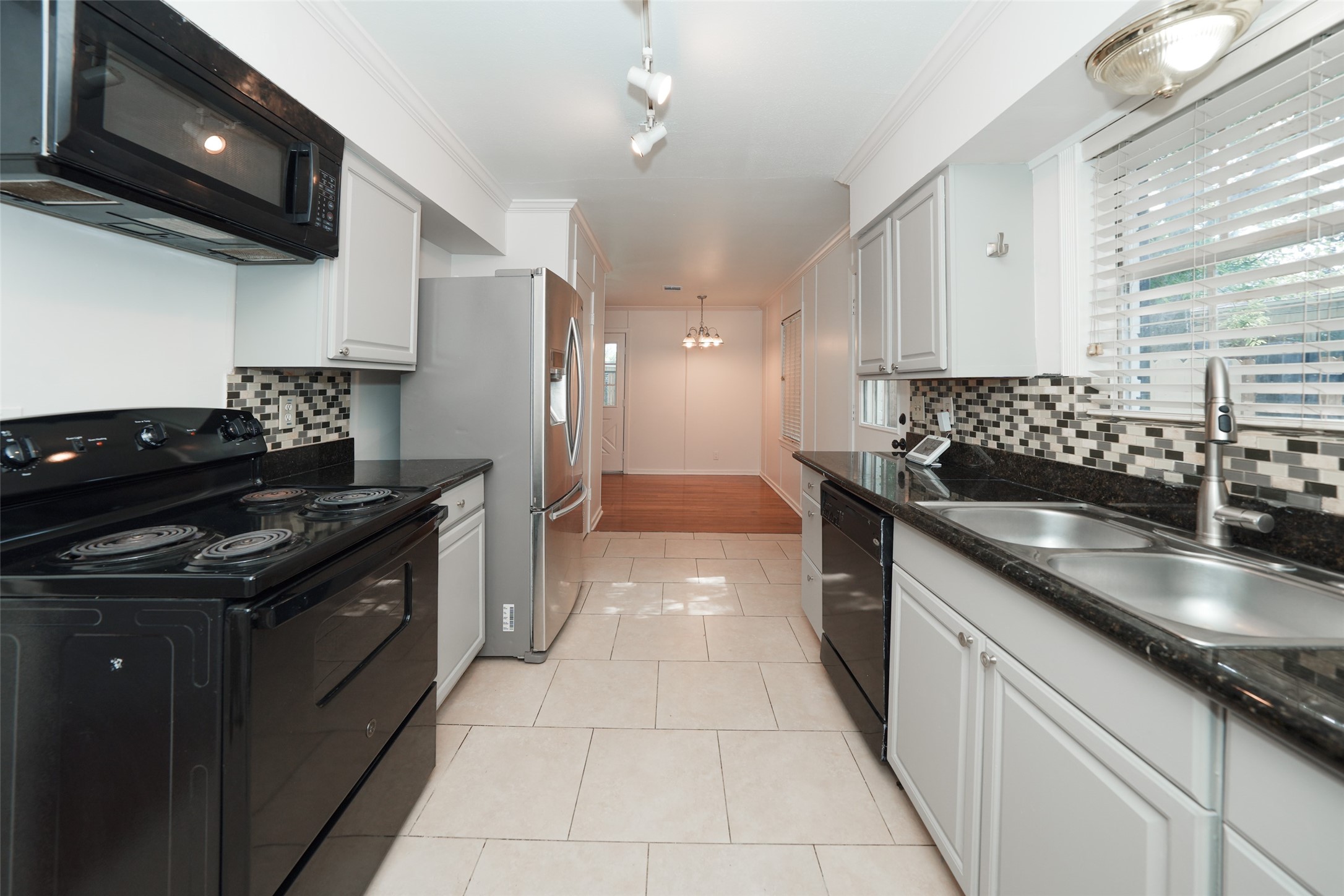9519 Val Verde Street Houston, TX 77063 - Photo 12 of 27 This kitchen features modern appliances, black countertops, and a stylish tile backsplash. It has bright white cabinetry, a double sink, and ample natural light from large windows, creating a welcoming and functional space.