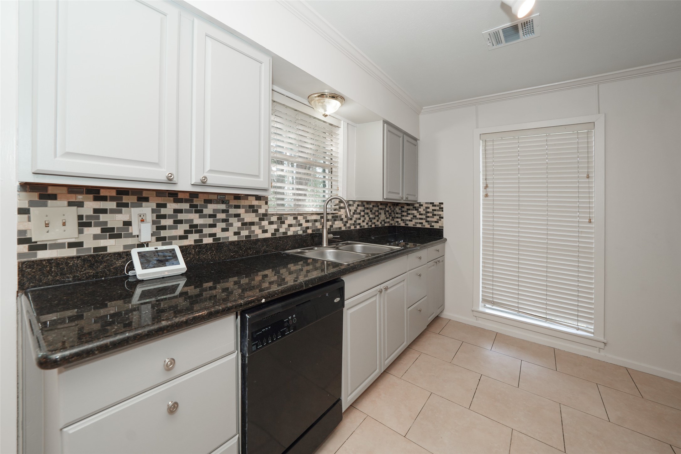 9519 Val Verde Street Houston, TX 77063 - Photo 15 of 27 Modern kitchen with sleek granite countertops, mosaic tile backsplash, and light cabinetry. Includes a double sink, black dishwasher, and ample natural light through a window with blinds.