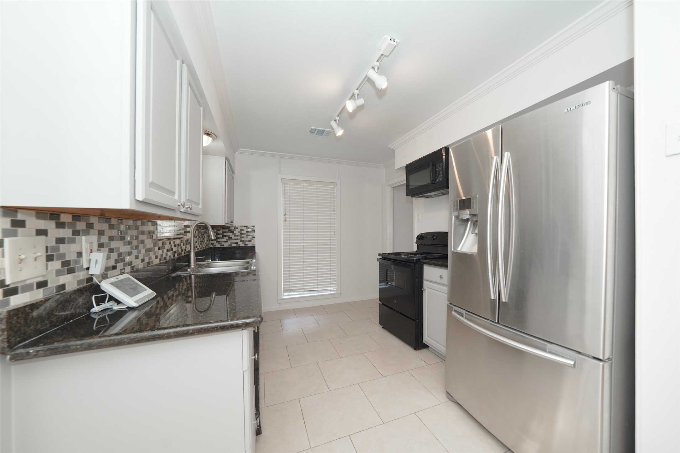 9519 Val Verde Street Houston, TX 77063 - Photo 16 of 27 This modern kitchen features sleek stainless steel appliances, granite countertops, and a stylish tile backsplash. It offers ample cabinet space and natural light, creating a bright and functional cooking area.