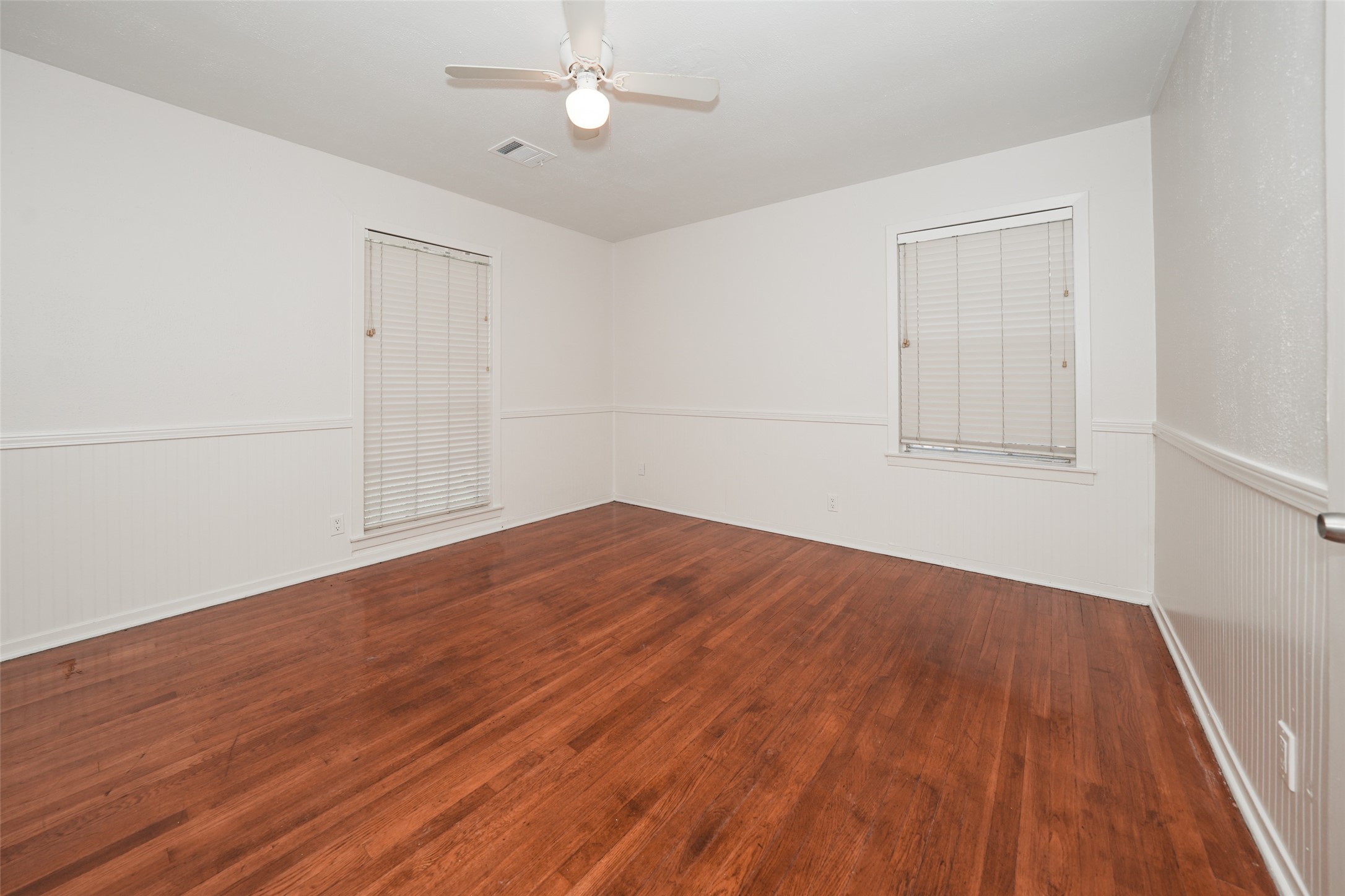 9519 Val Verde Street Houston, TX 77063 - Photo 18 of 27 This room features polished hardwood floors, neutral walls, and a ceiling fan, creating a bright and airy space perfect for a bedroom or office. The windows have blinds for privacy and light control.