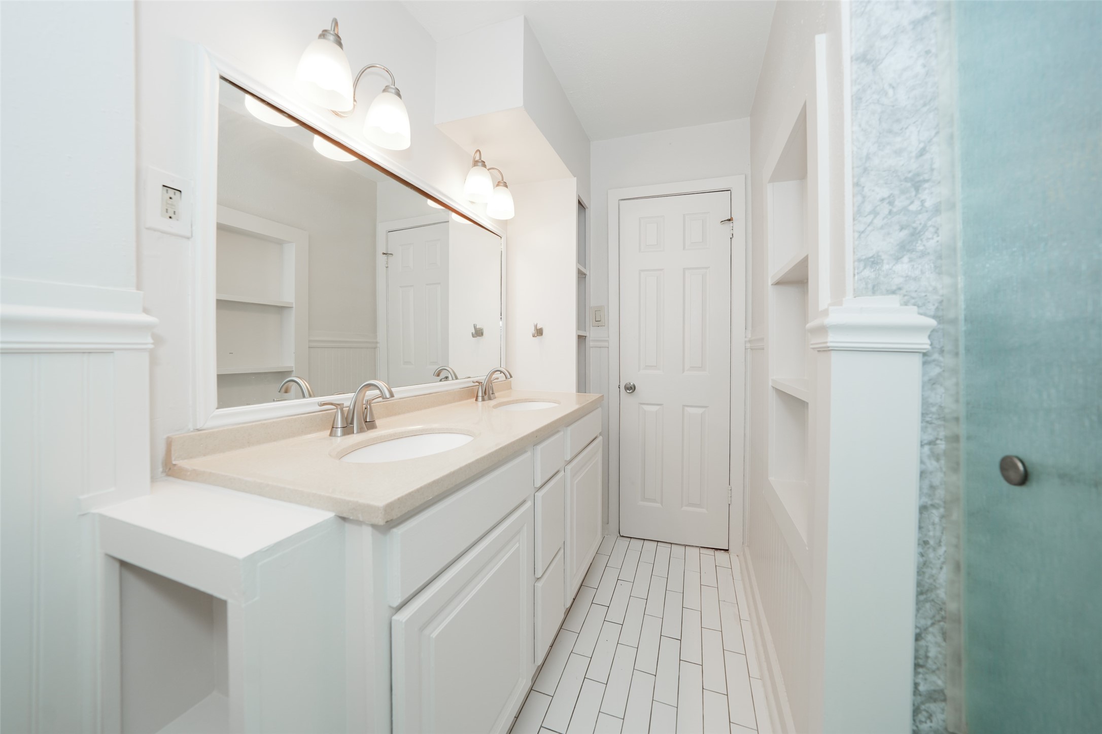 9519 Val Verde Street Houston, TX 77063 - Photo 21 of 27 This bright bathroom features a dual-sink vanity, modern fixtures, white tile flooring, ample storage with built-in shelves, and a frosted glass shower.