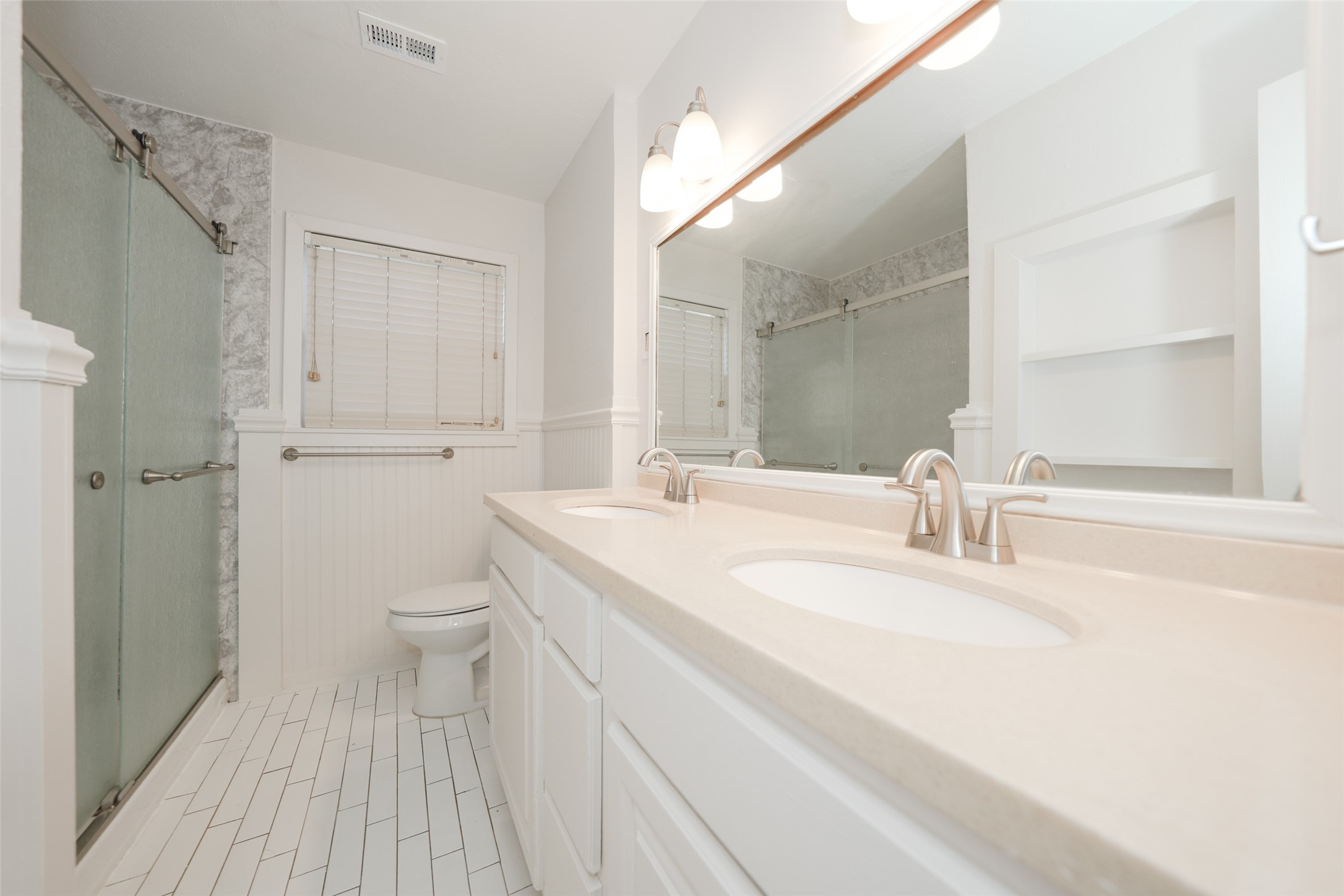 9519 Val Verde Street Houston, TX 77063 - Photo 22 of 27 This bathroom features a modern, clean design with a spacious double vanity, elegant light fixtures, and a large mirror. It includes a glass-enclosed shower and neutral tile flooring, creating a bright and inviting space.