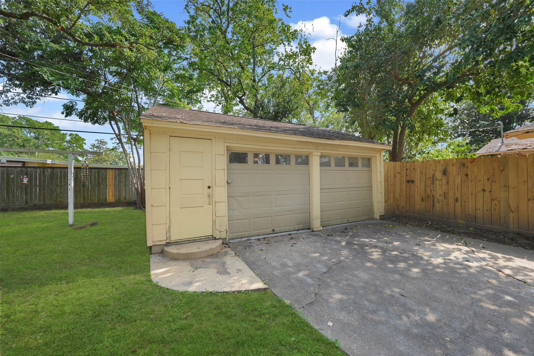 9519 Val Verde Street Houston, TX 77063 - Photo 23 of 27 This photo shows a two-car garage with a light yellow exterior, nestled in a fenced backyard. The surrounding area is spacious with green grass and mature trees, providing shade and privacy.