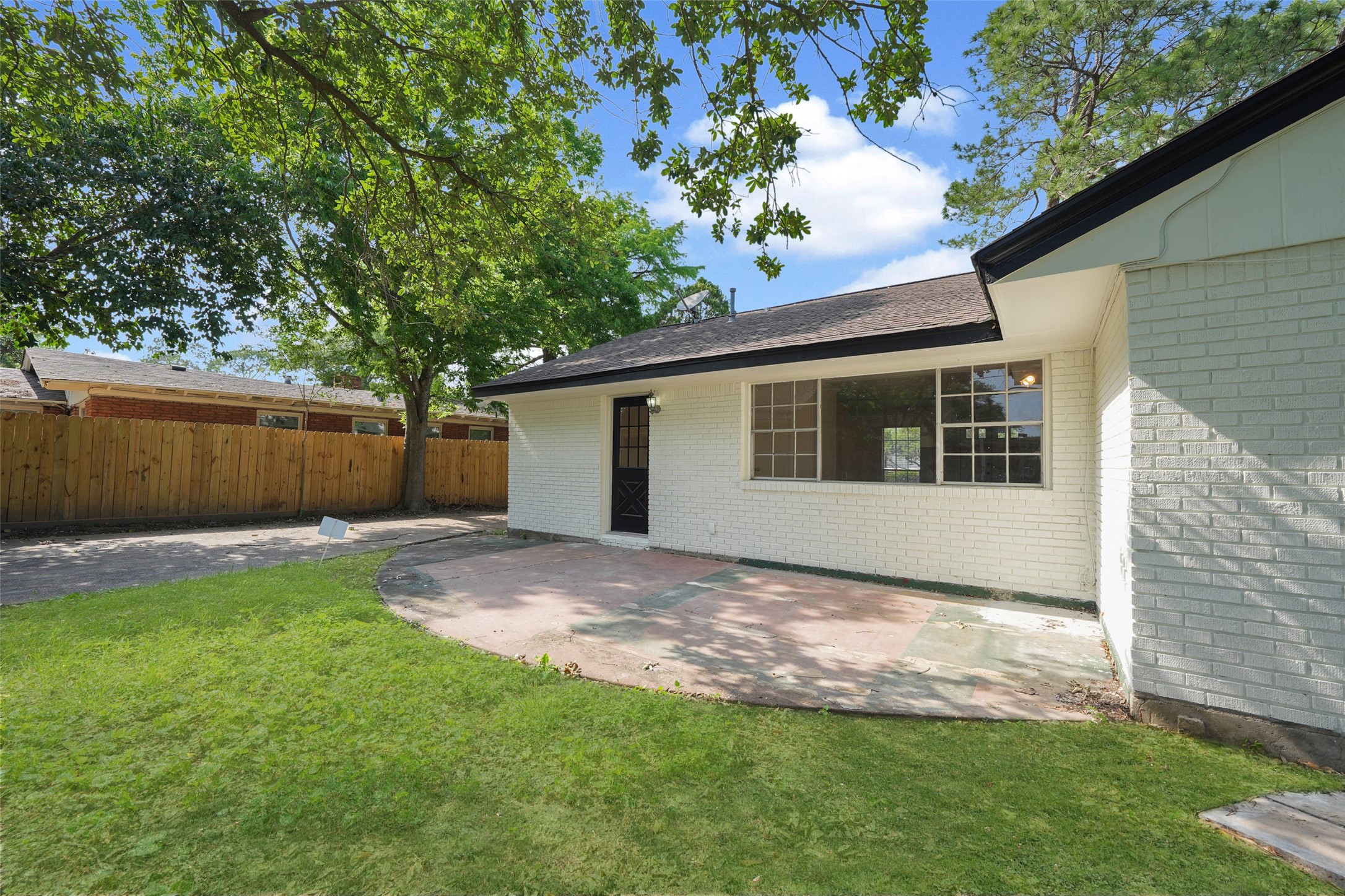 9519 Val Verde Street Houston, TX 77063 - Photo 24 of 27 Charming backyard with a spacious patio and lush lawn, surrounded by a wooden fence for privacy. The house features a white brick exterior and a large window for natural light. Perfect for outdoor relaxation and entertaining.