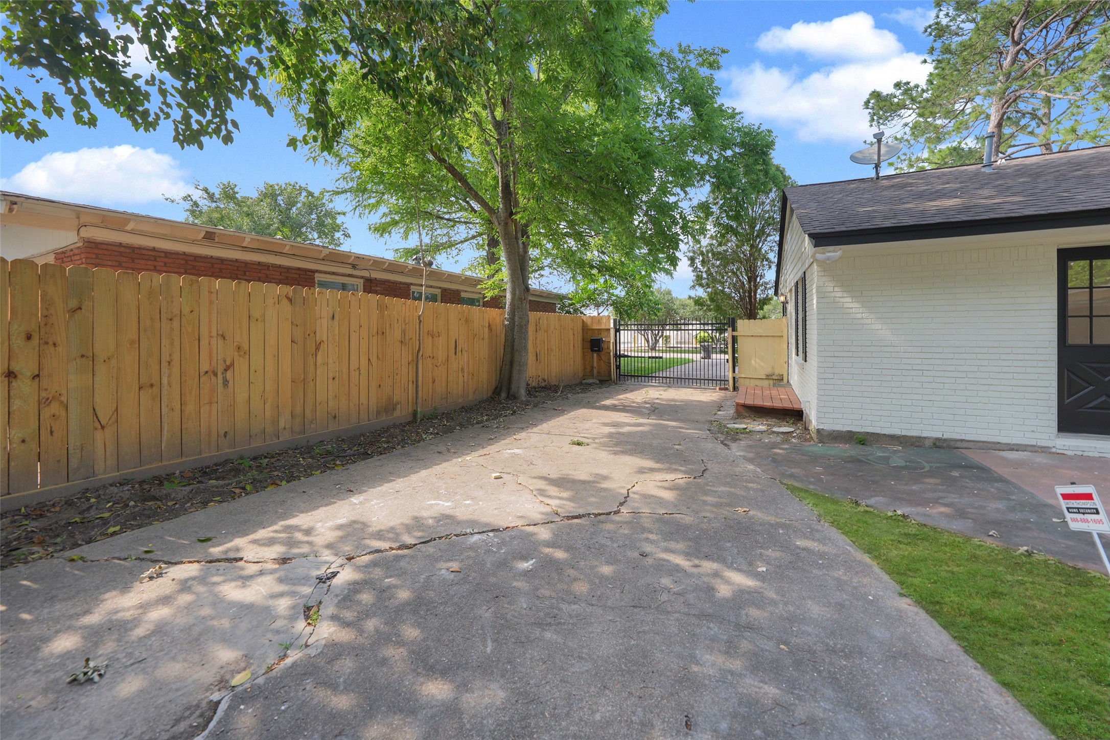 9519 Val Verde Street Houston, TX 77063 - Photo 25 of 27 A spacious driveway leads to a fenced backyard, offering privacy and potential for outdoor activities. The area is partially shaded by mature trees, providing a pleasant environment.