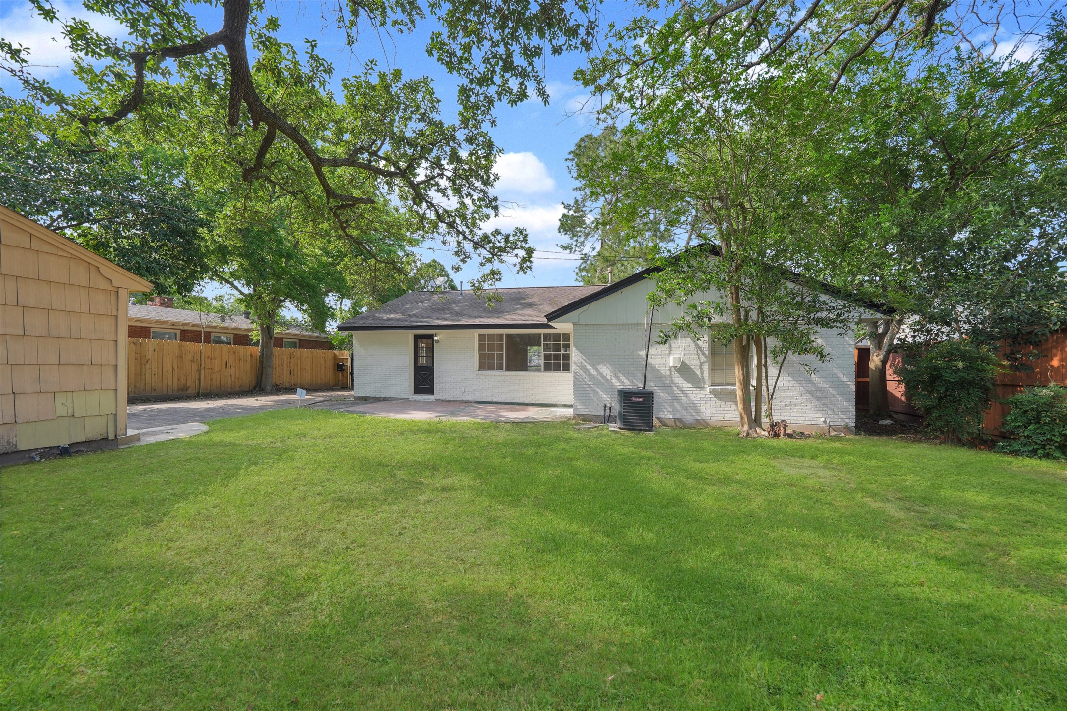 9519 Val Verde Street Houston, TX 77063 - Photo 26 of 27 Charming backyard with lush green lawn, mature trees providing shade, and a cozy white house. Perfect for outdoor activities and relaxation.