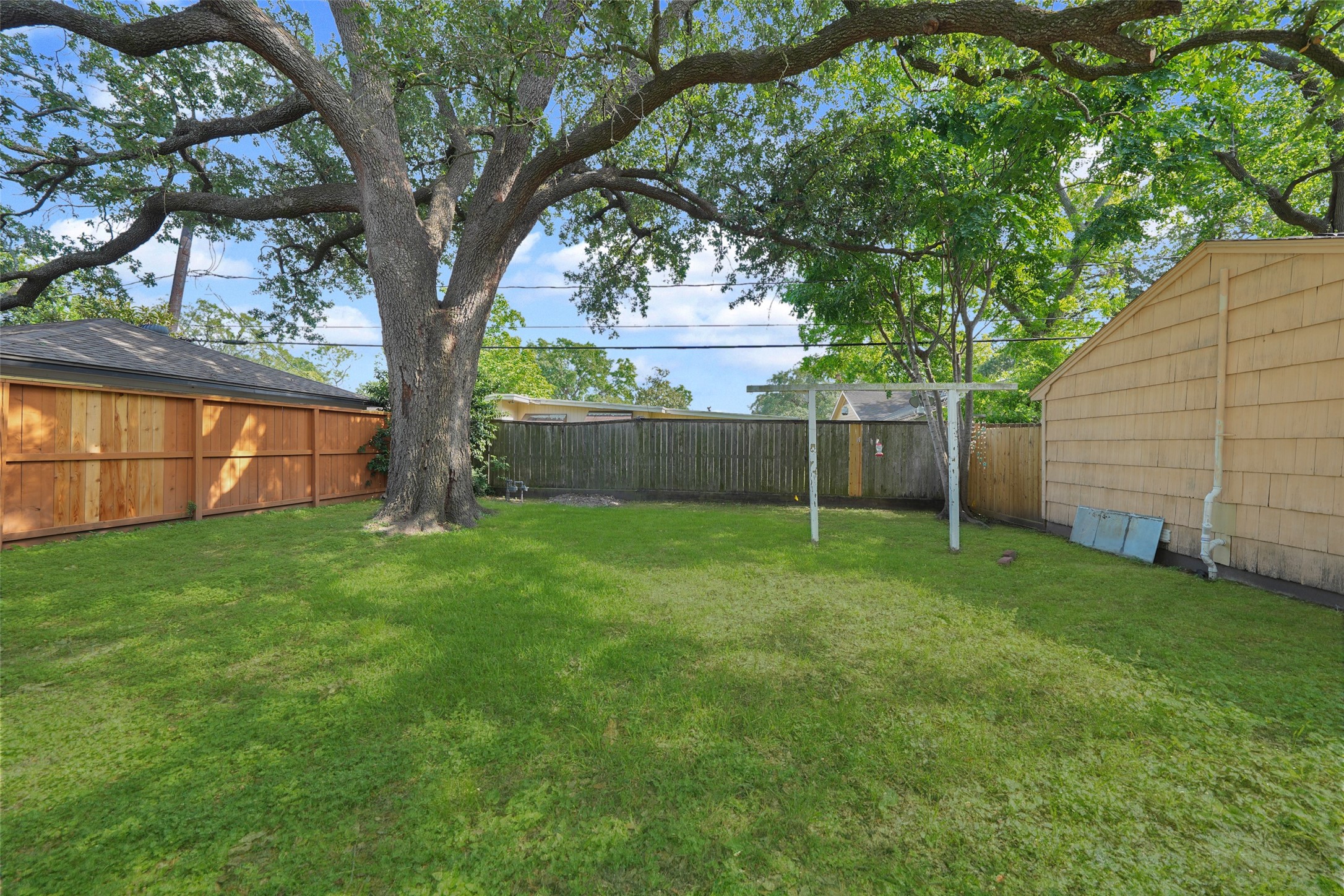 9519 Val Verde Street Houston, TX 77063 - Photo 27 of 27 Spacious backyard with lush grass, a large tree providing shade, and surrounded by a wooden fence. Ideal for outdoor activities and relaxation.