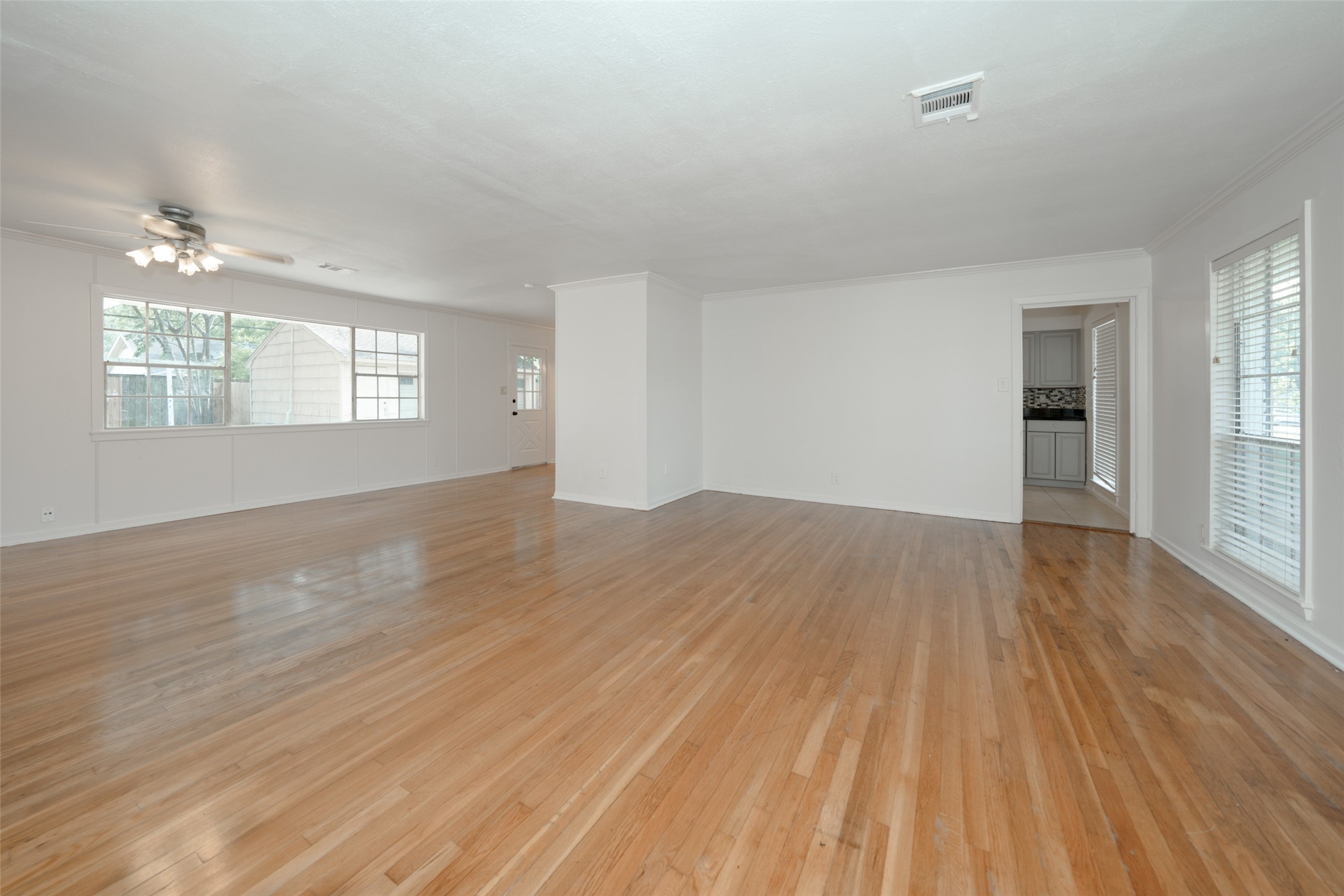 9519 Val Verde Street Houston, TX 77063 - Photo 4 of 27 Spacious, light-filled living area with polished hardwood floors, large windows, and a ceiling fan. The open layout leads to an adjacent room, perfect for versatile use.