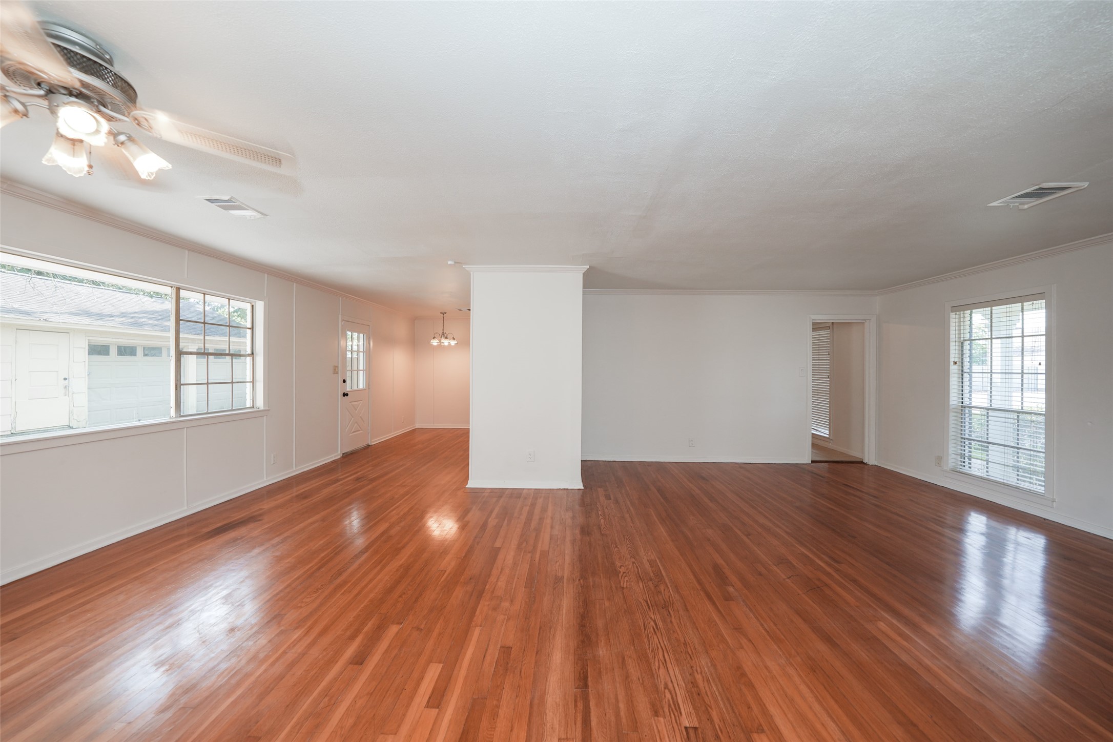 9519 Val Verde Street Houston, TX 77063 - Photo 5 of 27 This photo showcases a spacious living area with polished hardwood floors, large windows for natural light, and neutral-colored walls. The room has a ceiling fan and opens into an adjoining room, providing a versatile open-concept space.