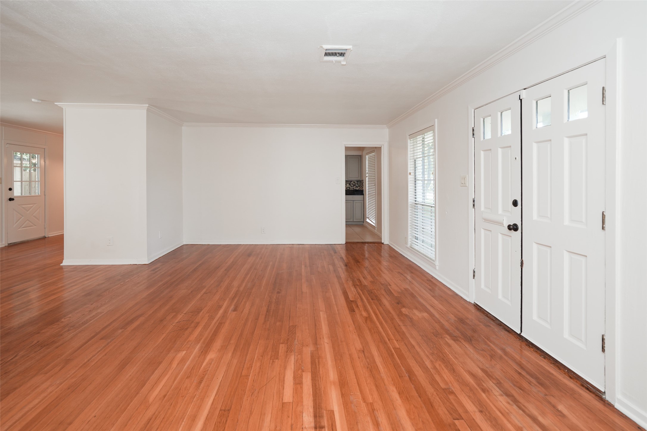 9519 Val Verde Street Houston, TX 77063 - Photo 6 of 27 This photo showcases a spacious, bright living room with hardwood floors, white walls, and a large front window. The room features a white front door and an open layout leading to the kitchen.