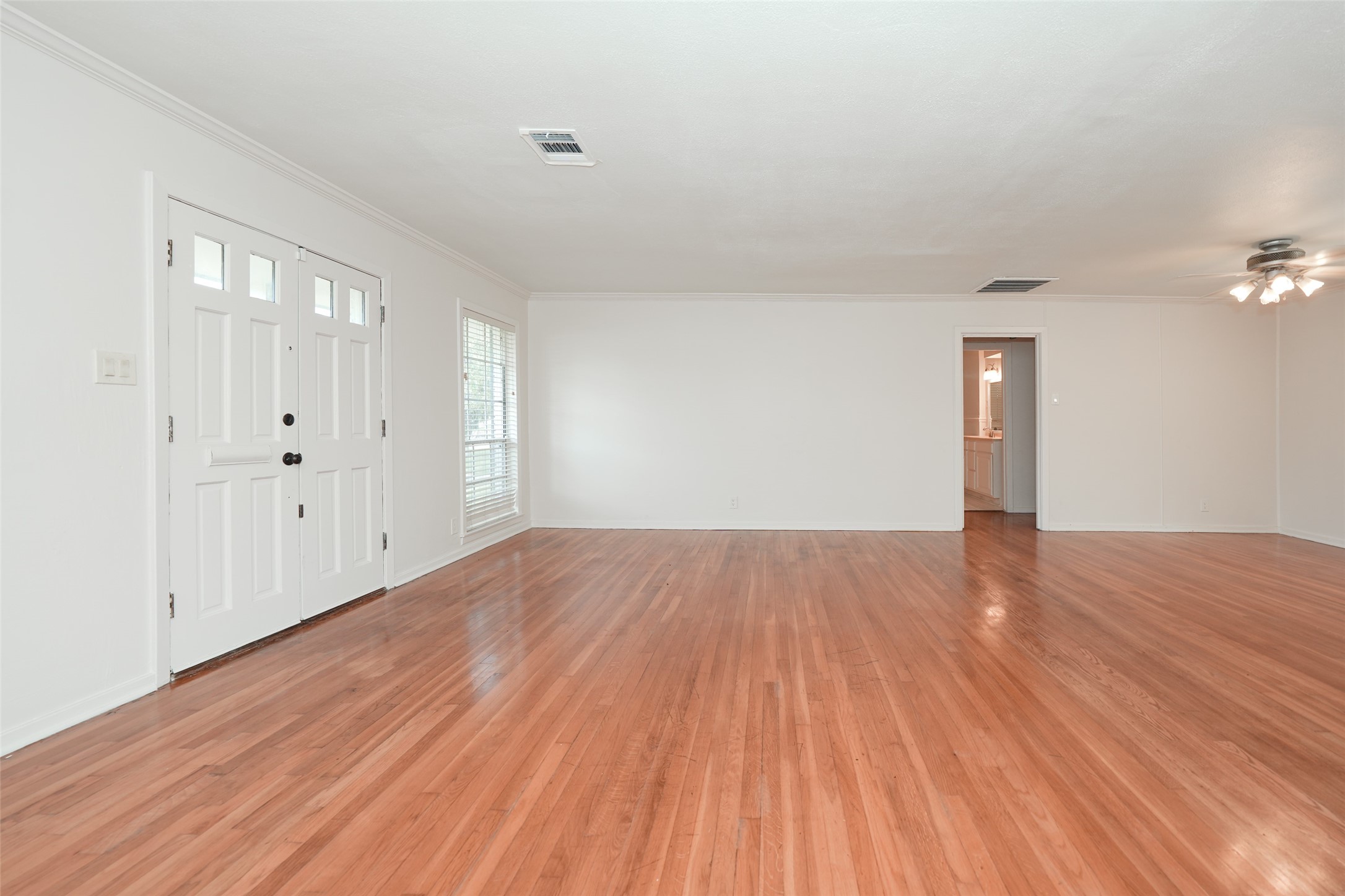 9519 Val Verde Street Houston, TX 77063 - Photo 7 of 27 Spacious living room with beautiful hardwood floors, neutral walls, and ample natural light from a large window. Features a ceiling fan and a view into the adjacent area, perfect for versatile living arrangements.