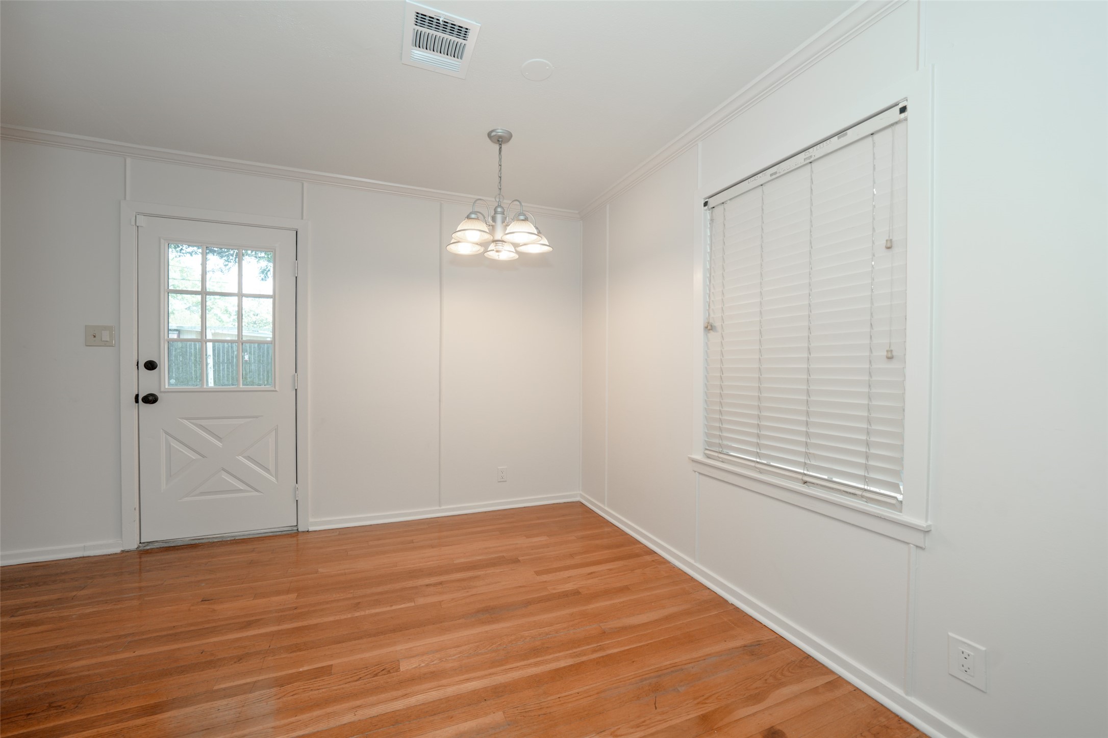 9519 Val Verde Street Houston, TX 77063 - Photo 8 of 27 Bright dining area with hardwood floors, white walls, and a ceiling light fixture. Features a window with blinds and a door leading outside, creating a cozy and inviting space.