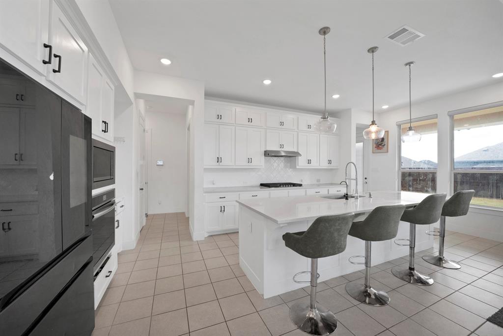 4222 Crown Run Road Midlothian, TX 76065 - Photo 7 of 40 White cabinetry with black hardware, tile flooring, kitchen island with built-in sink, stainless steel range hood, and multiple windows providing natural light