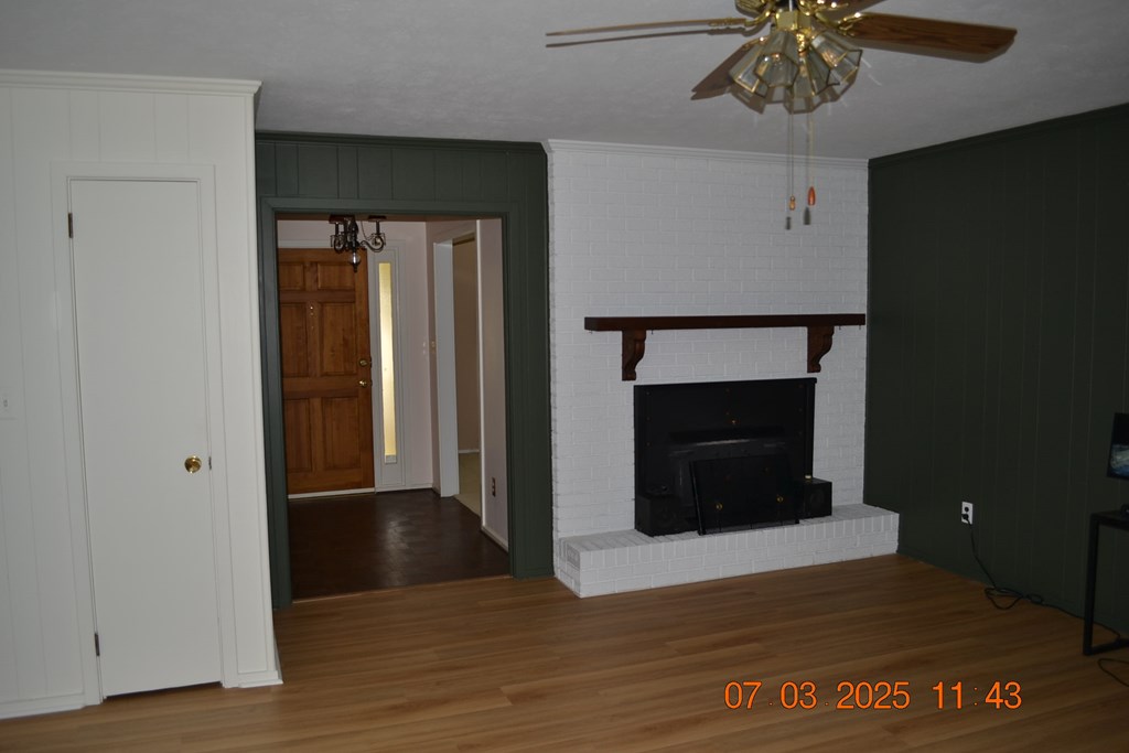 13642 Macon Road Upatoi, GA 31829 - Photo 5 of 34 an empty room with wooden floor a ceiling fan and a fireplace