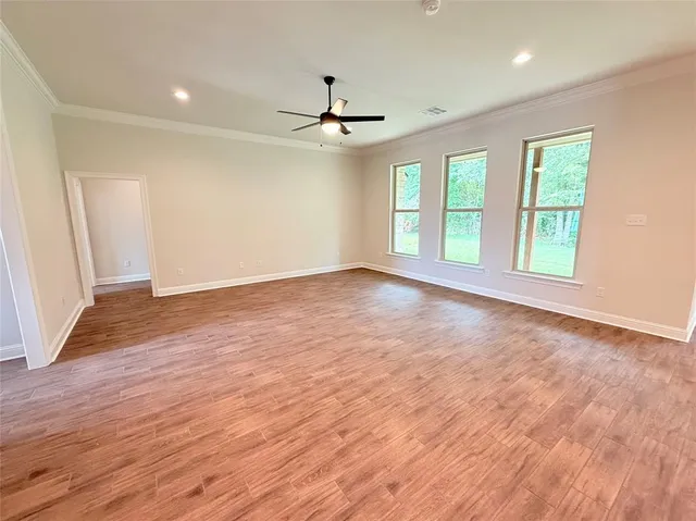 an empty room with wooden floor ceiling fan and windows