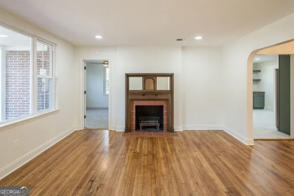 a view of an empty room with wooden floor fireplace and a window