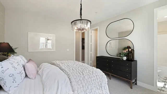 a bedroom with a bed mirror on dresser and a chandelier