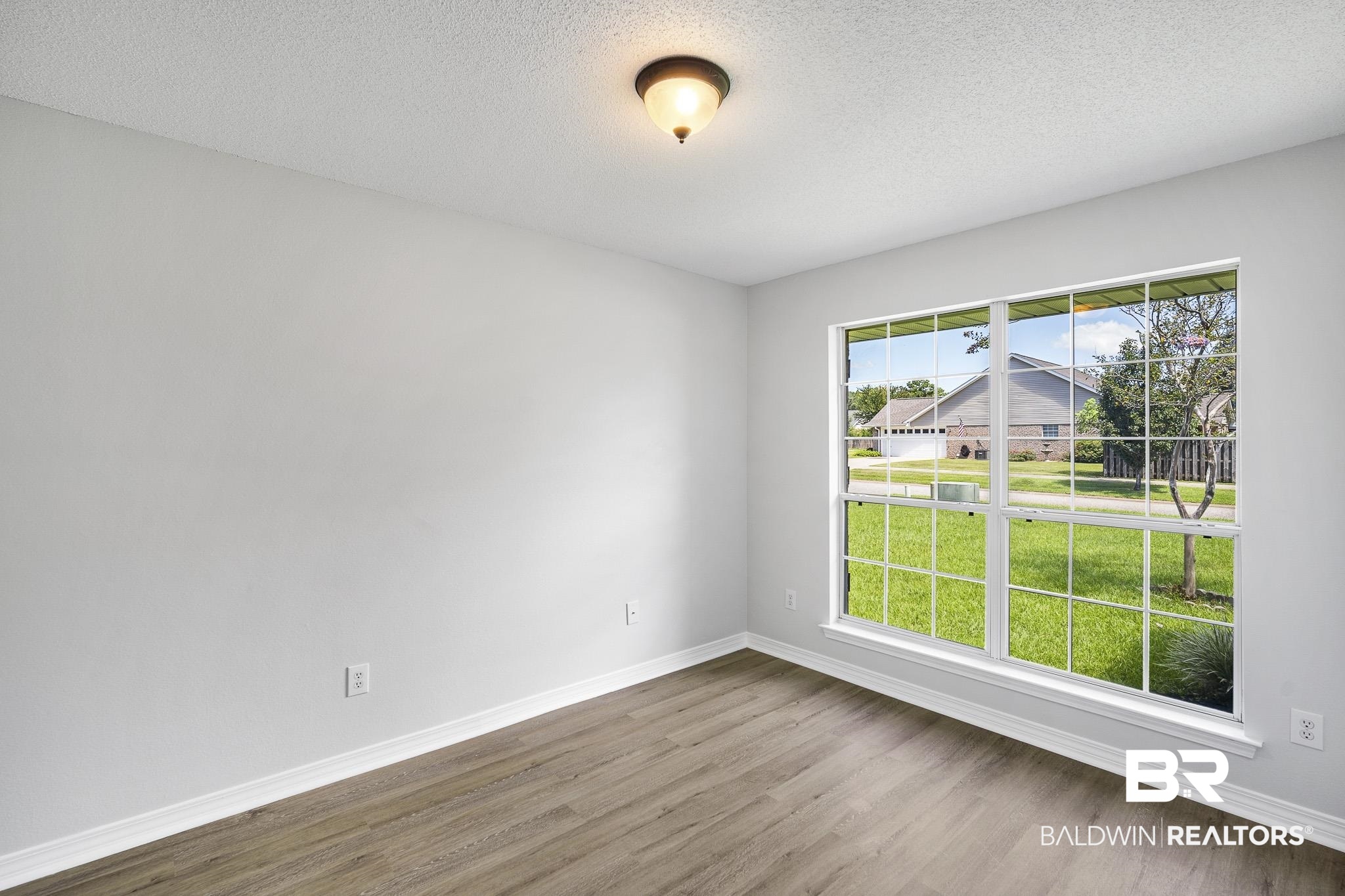9814 Woolrich Avenue Fairhope, AL 36532 - Photo 10 of 29 Empty room featuring a healthy amount of sunlight, wood-type flooring, and a textured ceiling