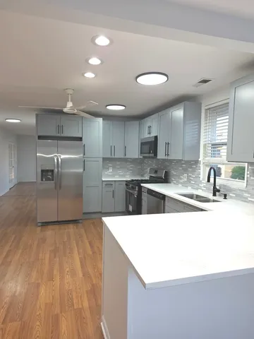 a view of a hallway to an empty room with wooden floor and a kitchen