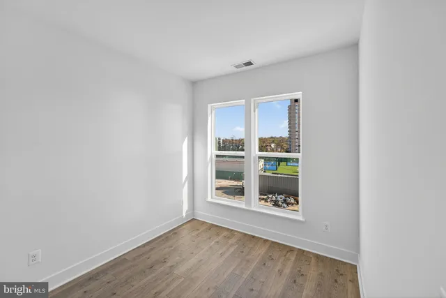 a view of an empty room with a window and hardwood floor