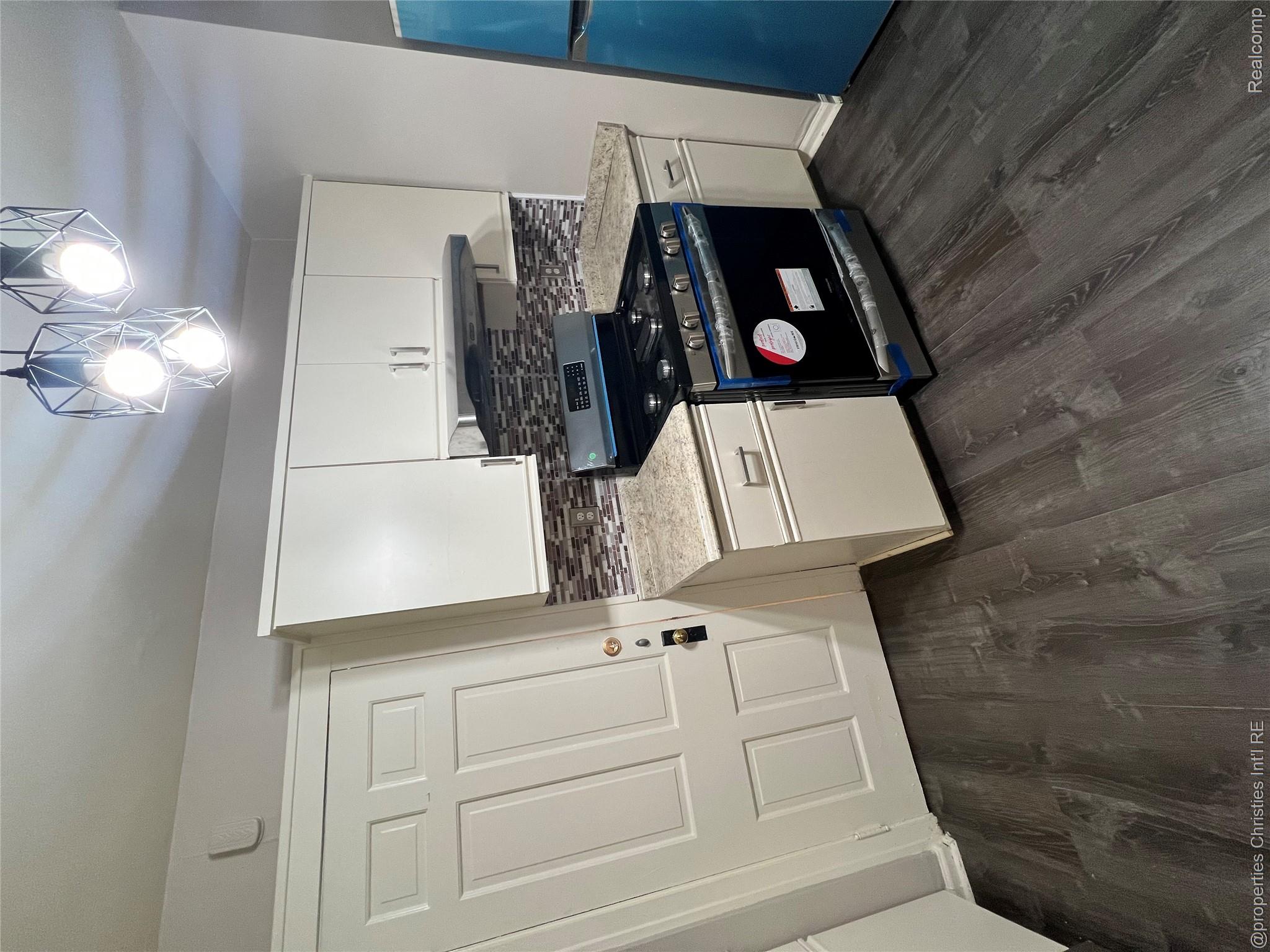 578 Neff Road Grosse Pointe, MI 48230 - Photo 4 of 16 White cabinetry with brushed nickel hardware, stone-finish countertops, geometric tile backsplash, and dark wood-finish flooring