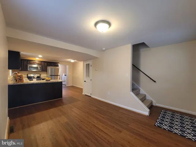 a view of an empty room with wooden floor and a kitchen