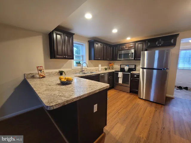 a kitchen with stainless steel appliances granite countertop a sink dishwasher a refrigerator and a stove with wooden floor