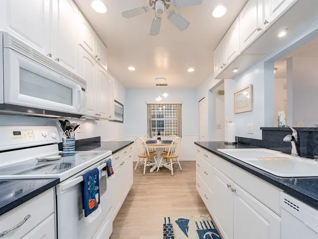 a large white kitchen with stainless steel appliances granite countertop a stove oven a sink dishwasher and cabinets with wooden floor