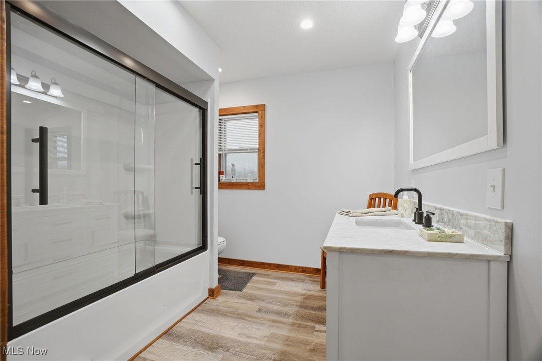Full bath with double vanity, combined bath / shower with glass door, light wood finished floors, and recessed lighting