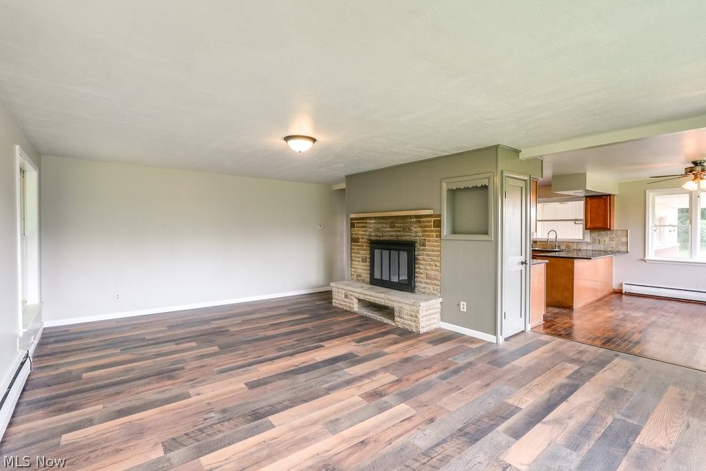 7105 Infirmary Road Ravenna, OH 44266 - Photo 13 of 33 Unfurnished living room with ceiling fan, hardwood / wood-style floors, sink, a baseboard heating unit, and a stone fireplace