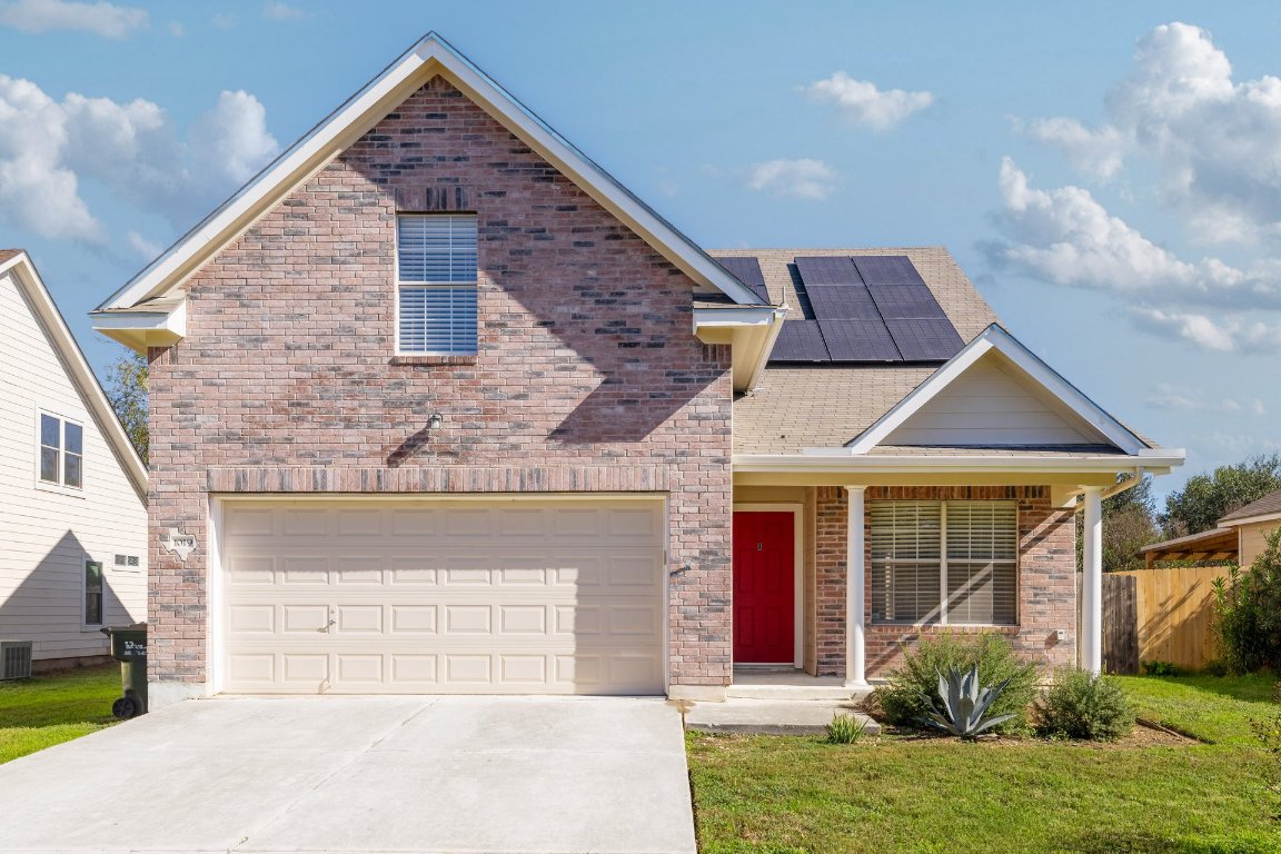 Traditional-style home featuring a porch, driveway, brick siding, roof mounted solar panels, and a garage