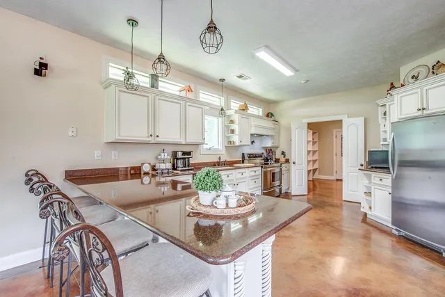 a kitchen with stainless steel appliances kitchen island granite countertop a stove a refrigerator a sink a dining table and chairs with white cabinets