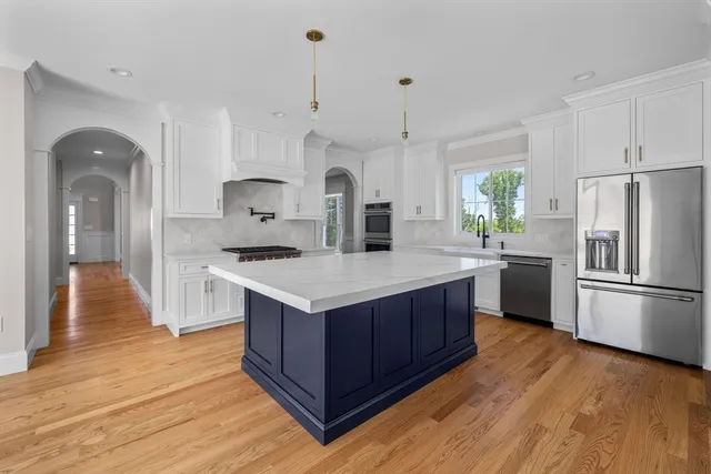 a kitchen with stainless steel appliances granite countertop a sink a stove a refrigerator and island with wooden floor